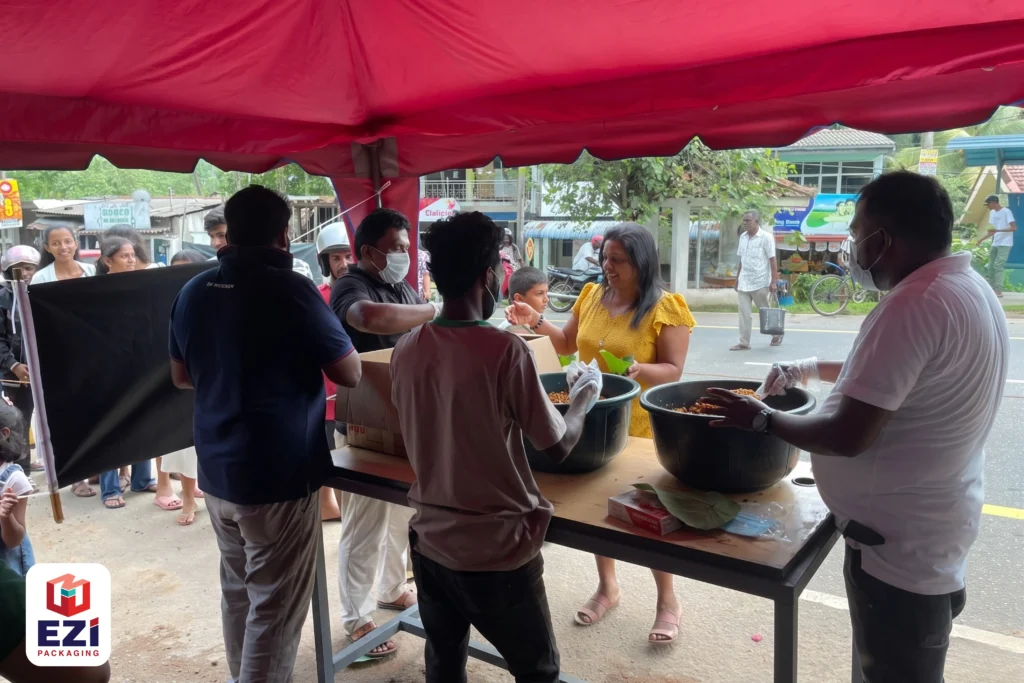 EZI Packaging volunteers working together behind a distribution counter to serve meals during a Vesak Poya dansala event