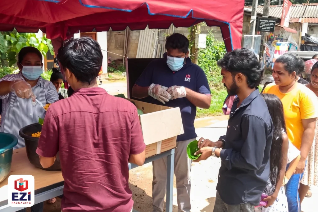 EZI Packaging staff member in a branded shirt serving food into eco-friendly plates for community members at the dansala event